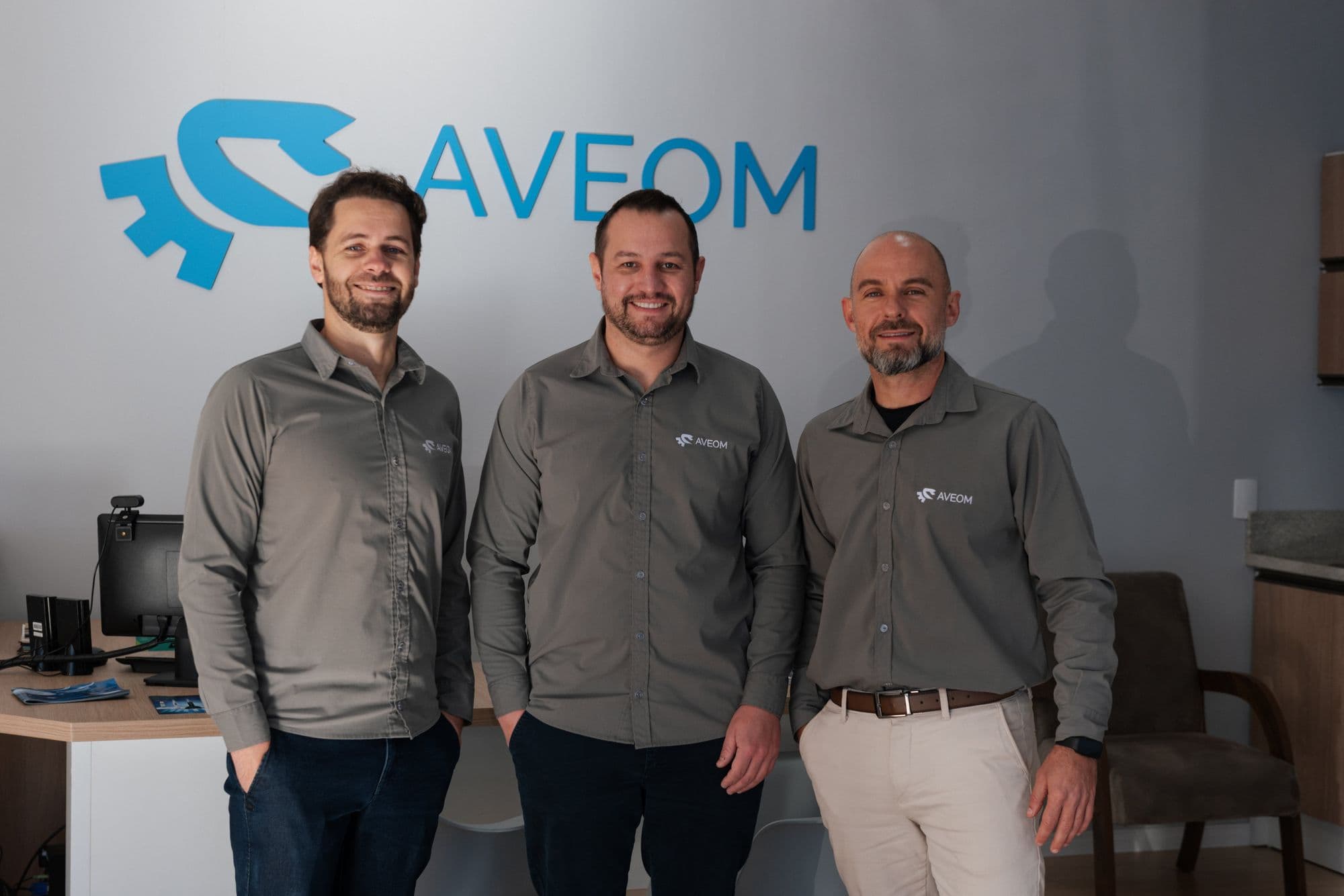 Equipe da Aveom em frente ao logotipo da empresa