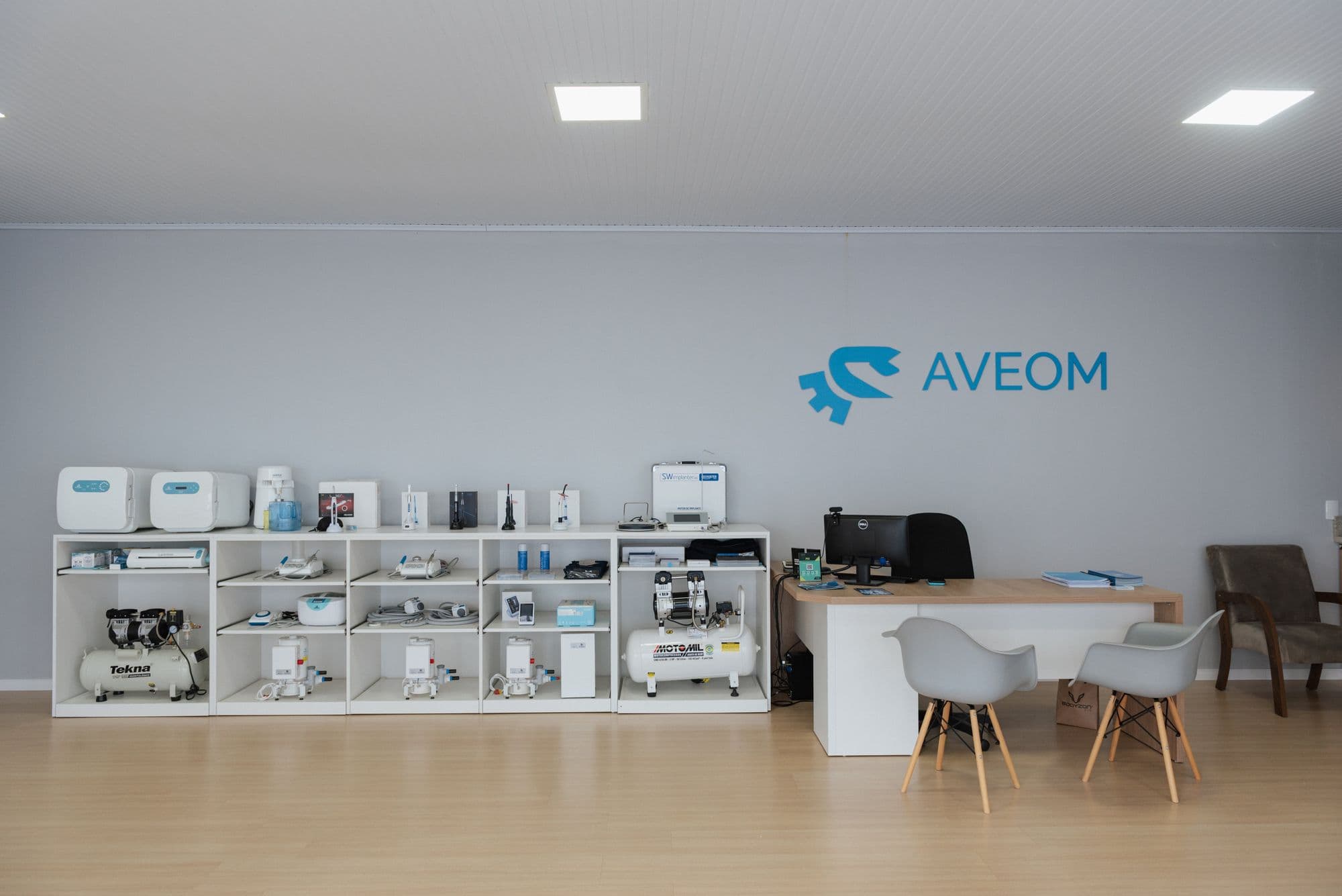 Showroom da Aveom com equipamentos odontológicos expostos e o logotipo na parede